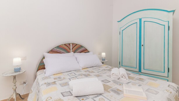 A bedroom with a bed, a nightstand, a lamp, a wardrobe, and a patterned headboard. - La Dimora Di Montelittu With AC (Loiri Porto San Paolo)