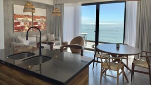Een moderne keuken met een centraal eiland, een eetgedeelte met een ronde tafel en uitzicht op zee door grote ramen.
