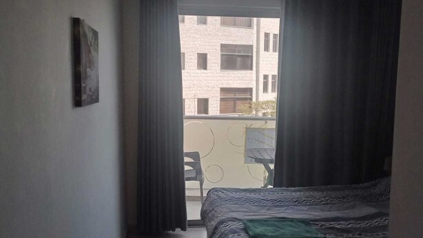 A bedroom with a bed, a view of a building through a window, and a chair outside. - Overlooking studio in Abdoun near UN offices with serviced area (AMMAN)