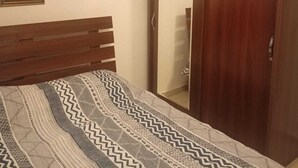 A bedroom with a wooden bed frame, a patterned bedspread, a wardrobe with a mirror, and a framed picture on the wall. - Overlooking studio in Abdoun near UN offices with serviced area (AMMAN)