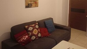A living room with a dark brown sofa, two patterned cushions, a wall-mounted air conditioner, and a door to the right. - Overlooking studio in Abdoun near UN offices with serviced area (AMMAN)