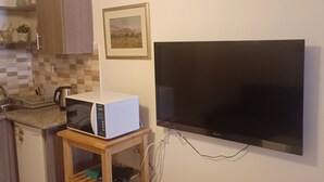 A compact kitchen with a microwave, a sink, and a wooden shelf unit. - Overlooking studio in Abdoun near UN offices with serviced area (AMMAN)