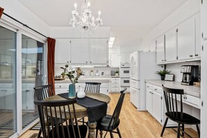 A modern kitchen with white cabinets, a chandelier, and a dining area with a table and chairs.