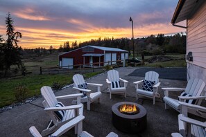 A patio with four Adirondack chairs and a fire pit, overlooking a red barn and a scenic sunset. - Estate Surrounded By Trees, Hills, and Farmland, w/ Fire-Pits, Air Hockey, Foosball, BBQ, Pet-Friend (Damascus)