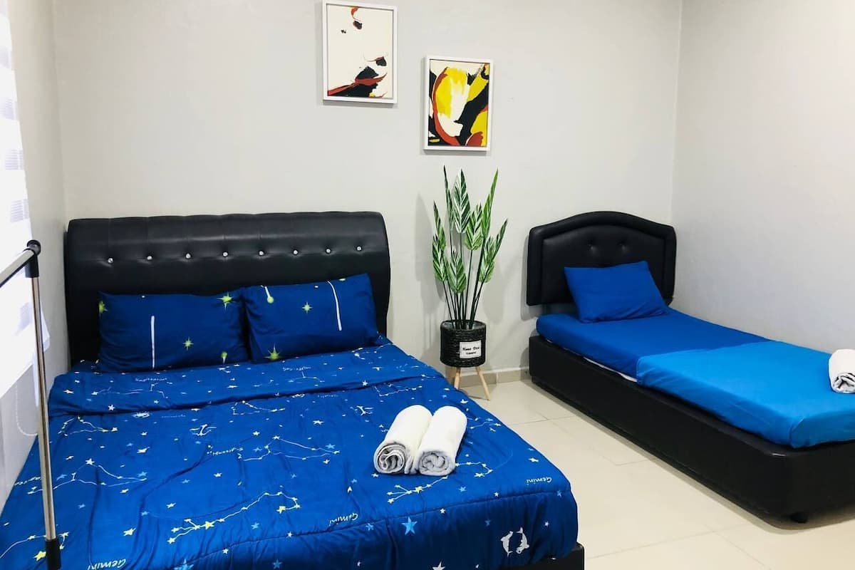 Quarto de hotel com uma cama grande, uma cama menor e uma mesa de cabeceira com uma planta.
