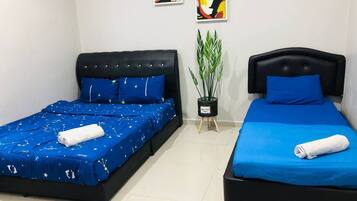 Two single beds with blue bedding and white towels, a potted plant, and two abstract paintings on the wall.
