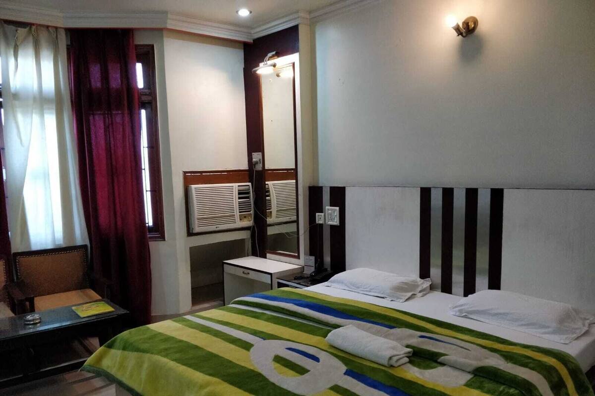 A hotel room with a bed, a desk, a chair, a mirror, and a window with curtains.