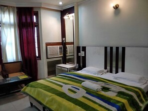A hotel room with a bed, a desk, a chair, a mirror, and a window with curtains.