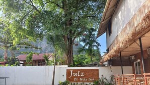 A sign for 'Julz El Nido Inn' with a white wall and wooden signboard, surrounded by greenery and outdoor seating. - Julz El Nido Inn by Cocotel (El Nido)