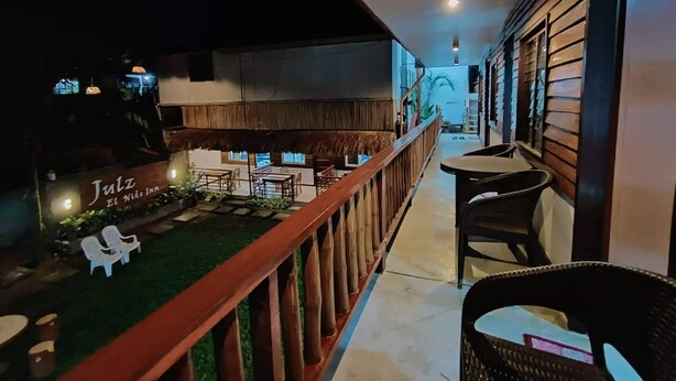 A hotel corridor with a wooden railing, outdoor seating area with tables and chairs, and a sign for 'Jutz El Nido Inn'. - Julz El Nido Inn by Cocotel (El Nido)