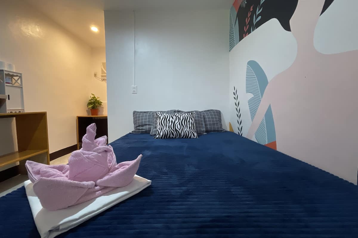 Une chambre d’hôtel avec un grand lit, une fresque murale, un petit bureau et une plante en pot.