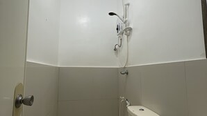 A small, clean bathroom with a toilet, a green trash bin, and a shower with a handheld showerhead. - Julz El Nido Inn by Cocotel (El Nido)