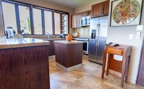 A kitchen with dark wood cabinets, a granite countertop, a stainless steel refrigerator, and a microwave. - Sweeping Banderas Bay Views, Rooftop Pool & Bar - Residences by Pinnacle Unit 20 (Puerto Vallarta)