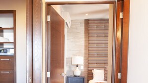 A hotel room with a bed, bedside table, lamp, and a view of the hallway. - Sweeping Banderas Bay Views, Rooftop Pool & Bar - Residences by Pinnacle Unit 20 (Puerto Vallarta)