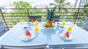 A table set with a pineapple, watermelon slices, and drinks, overlooking a cityscape. - Sweeping Banderas Bay Views, Rooftop Pool & Bar - Residences by Pinnacle Unit 20 (Puerto Vallarta)