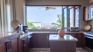 A kitchen with a large island, dark wood cabinets, a built-in oven, and a view of palm trees and buildings outside. - Sweeping Banderas Bay Views, Rooftop Pool & Bar - Residences by Pinnacle Unit 20 (Puerto Vallarta)