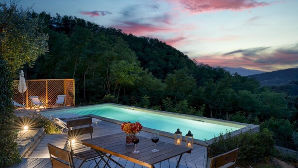Una piscina privada con cubierta de madera, sillas de descanso y una mesa con bebidas y flores.