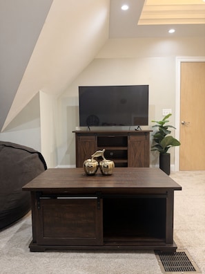 A living room with a dark wooden coffee table, a flat-screen TV on a wooden stand, and a potted plant.