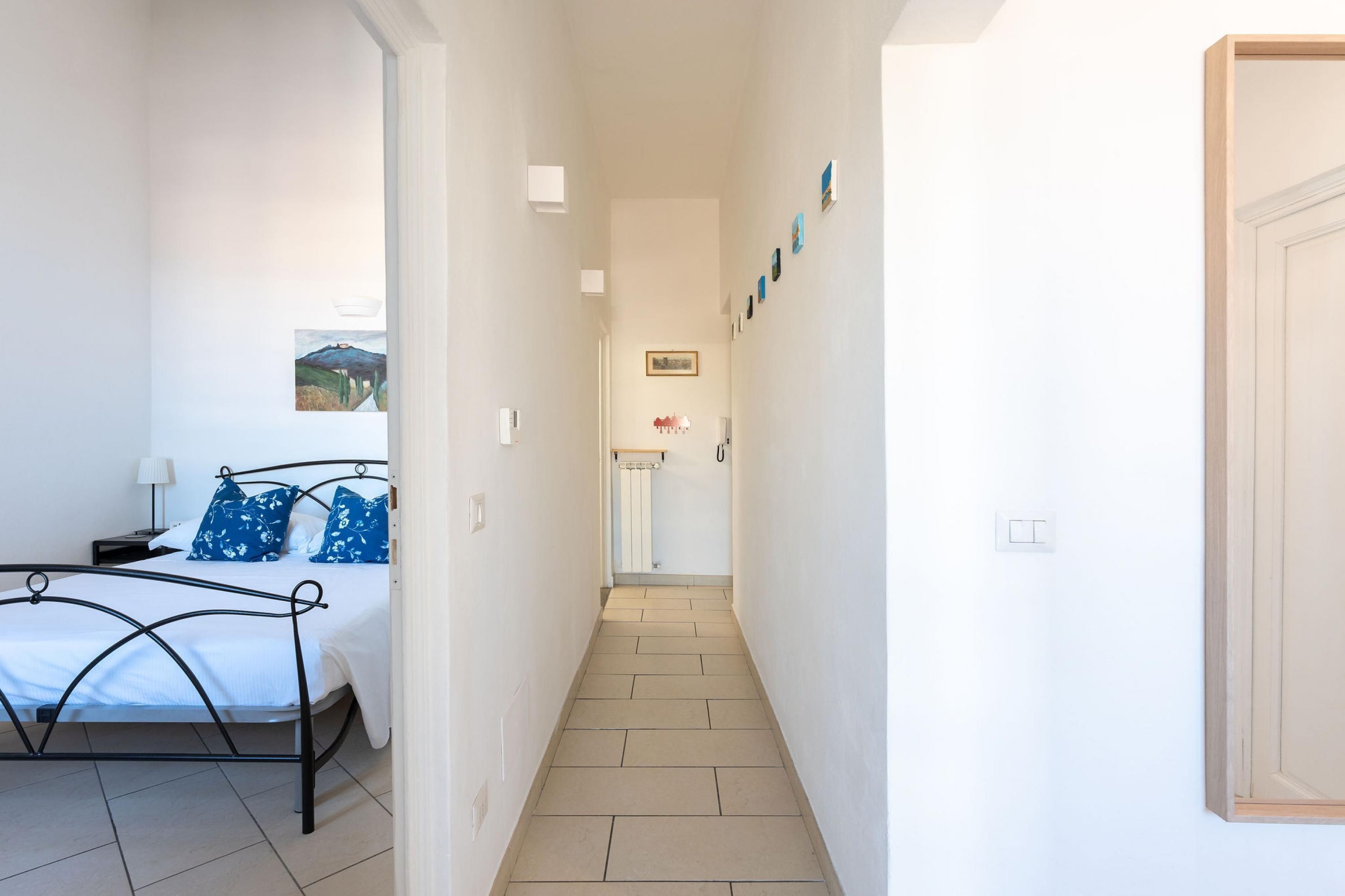 A narrow hallway with a bed on the left, a radiator in the center, and a door on the right.