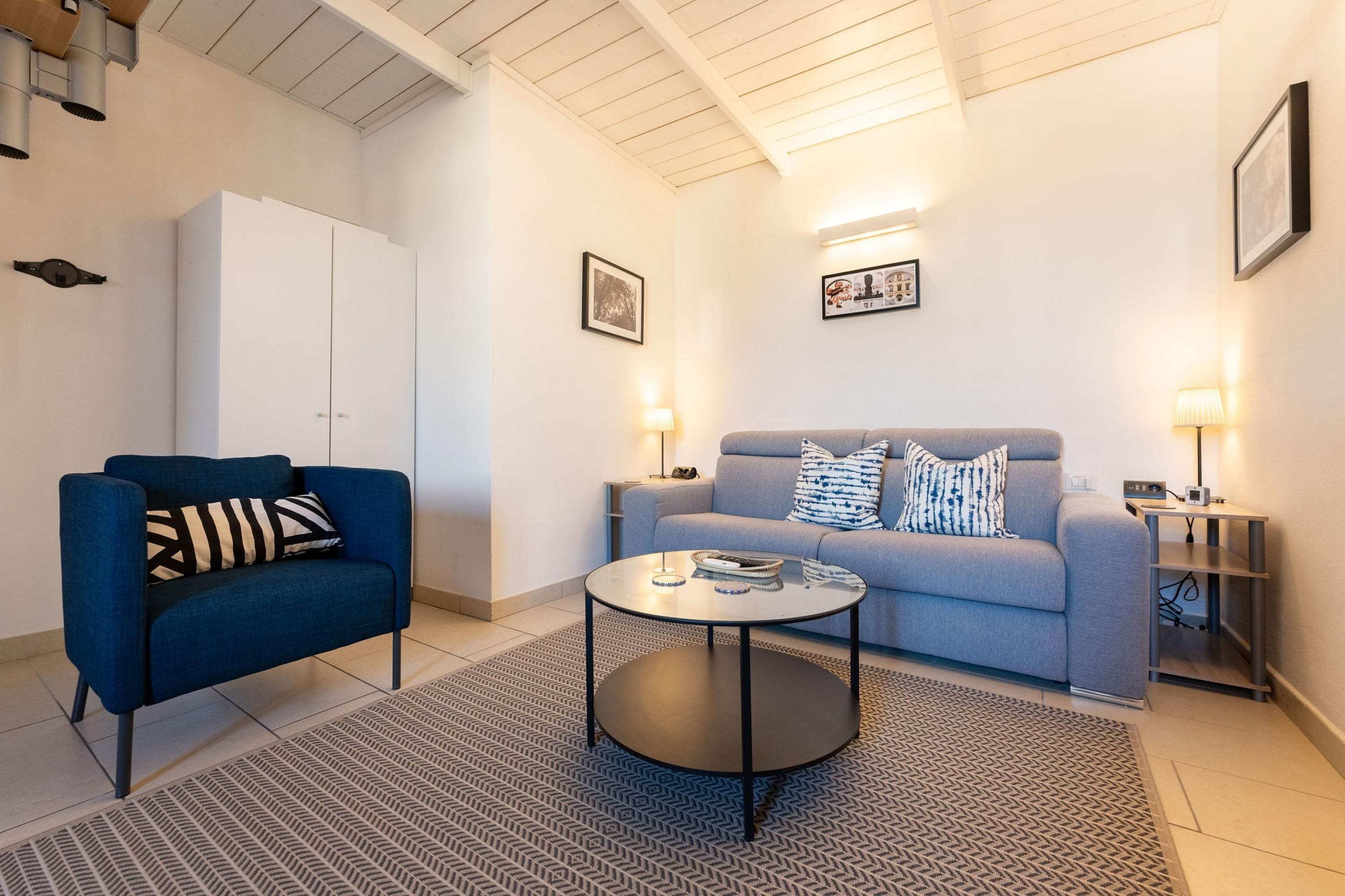 A modern living room with a blue sofa, a blue armchair, a round coffee table, and a white cabinet.