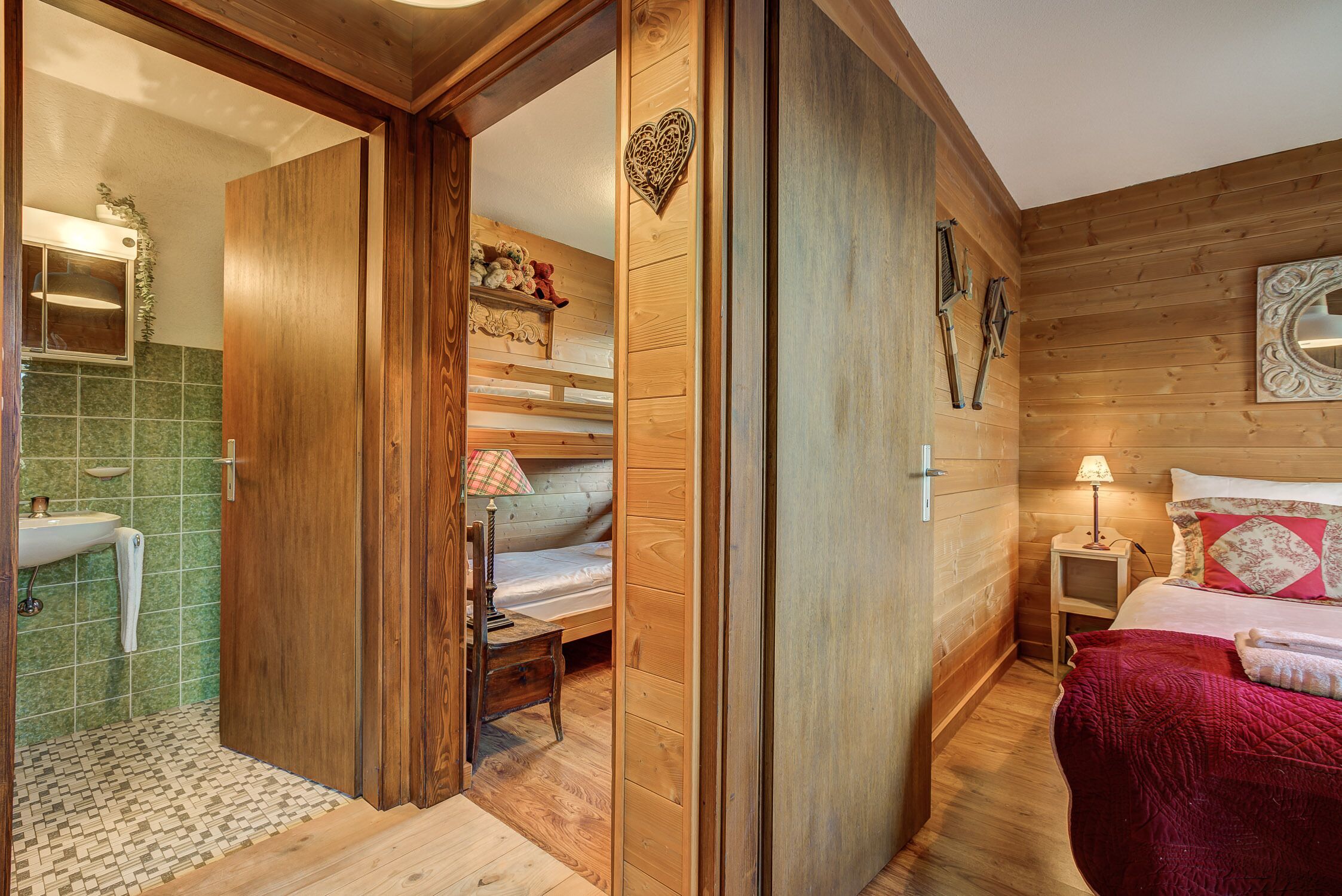 L’intérieur d’une cabane en bois comprend une salle de bain, un lit superposé, une table de chevet avec une lampe et un lit recouvert d’une couverture rouge.