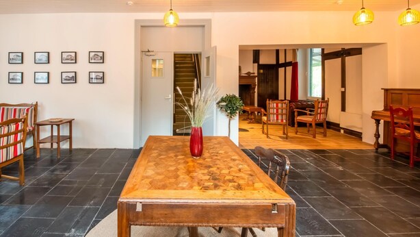 A spacious dining area with a wooden table and chairs, a red vase with dried plants, and framed pictures on the wall.