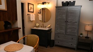 Ein Badezimmer mit einem Holzkabinent, einem runden Spiegel, einem Waschbecken mit einer Blumenvase und einem Stuhl mit Untersetzer.