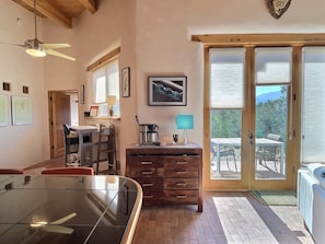 A dining area with a glass table, wooden chairs, a coffee maker, and a view through a sliding glass door to an outdoor patio.