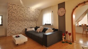 Ein Wohnzimmer mit einer Wand mit Muster, einem Sofa, einem Couchtisch, einer Uhr und einem Fenster mit Vorhängen.