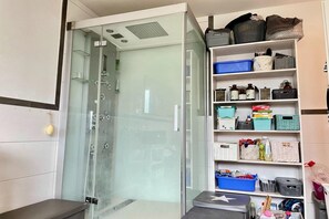 A bathroom with a glass shower enclosure, a white sink, and a shelf with storage bins and toiletries.