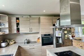 Cozinha moderna com armários de madeira clara, eletrodomésticos de aço inoxidável e uma parede de tijolos decorativa.