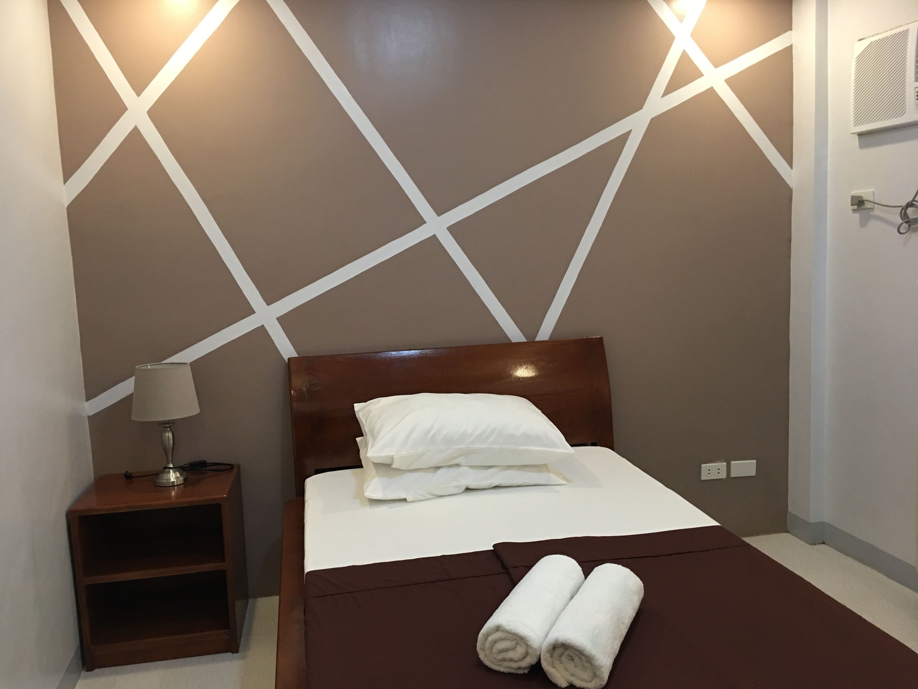 A neatly made bed with white linens, a brown headboard, and two rolled towels on the bed.