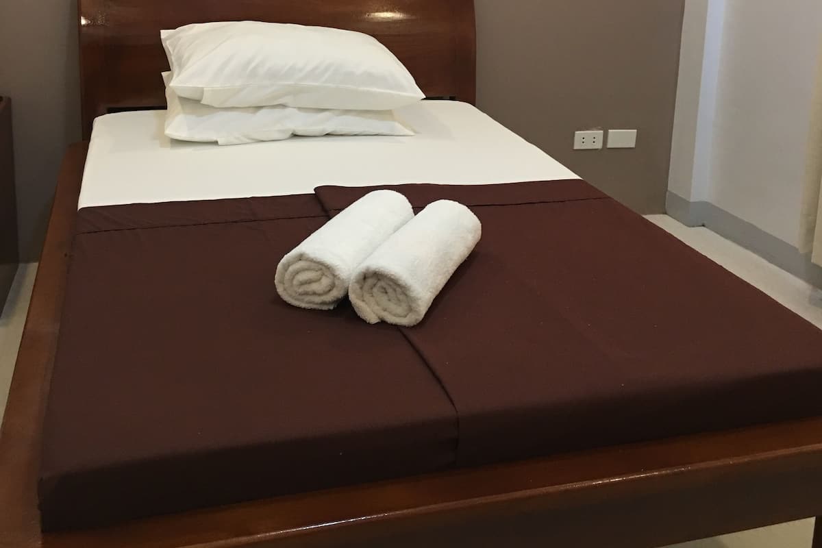 A neatly made bed with a brown headboard, white pillows, and two rolled towels on a brown bedspread.
