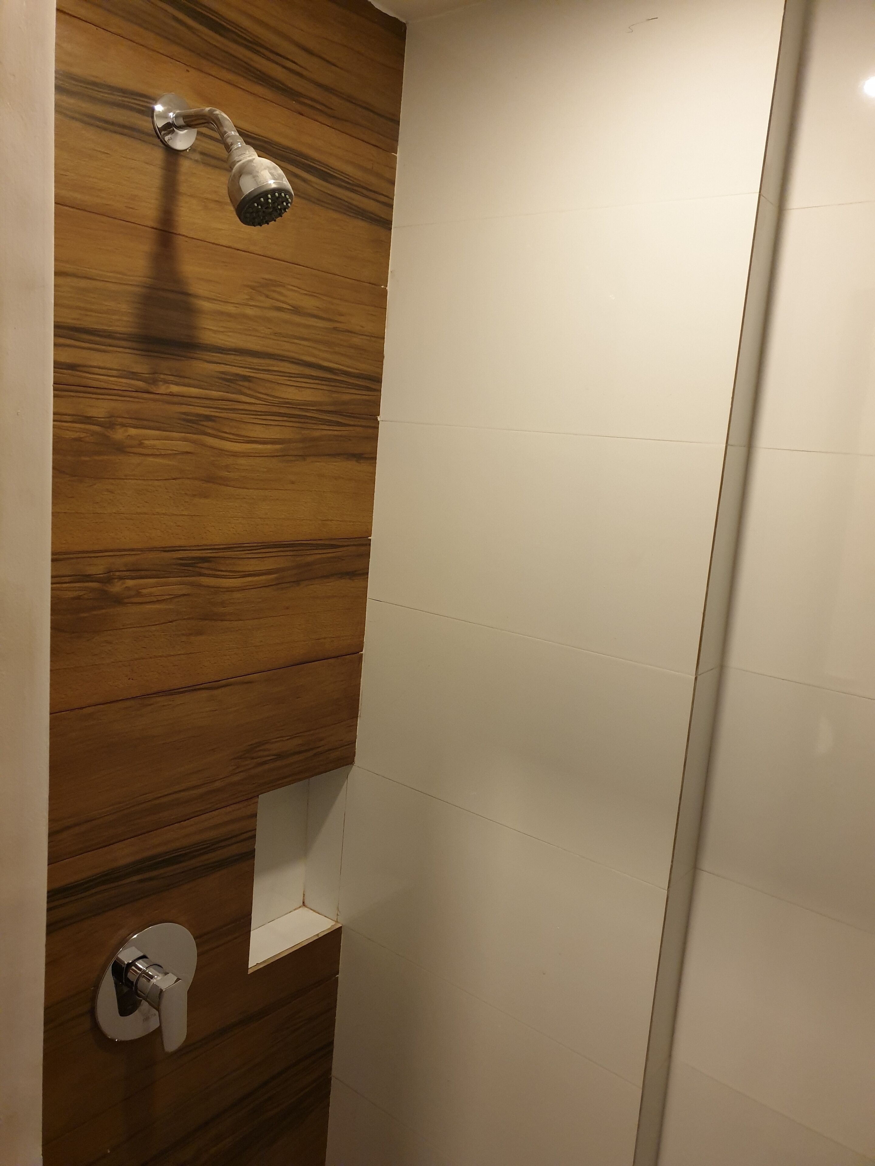 Ducha con pared de paneles de madera, pared de azulejos blancos y puerta blanca.