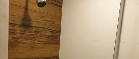 Ducha con pared de paneles de madera, pared de azulejos blancos y puerta blanca.