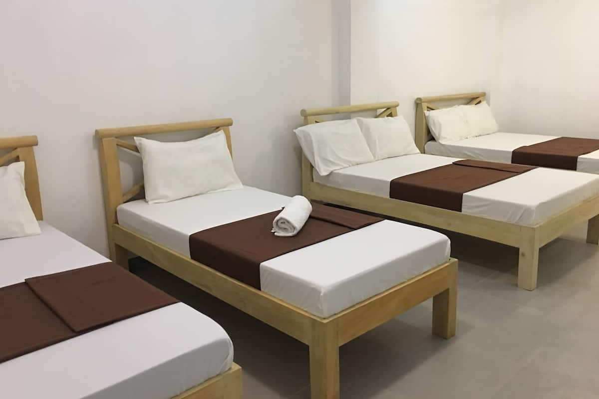A hotel room with four single beds, each with a wooden frame and white bedding.