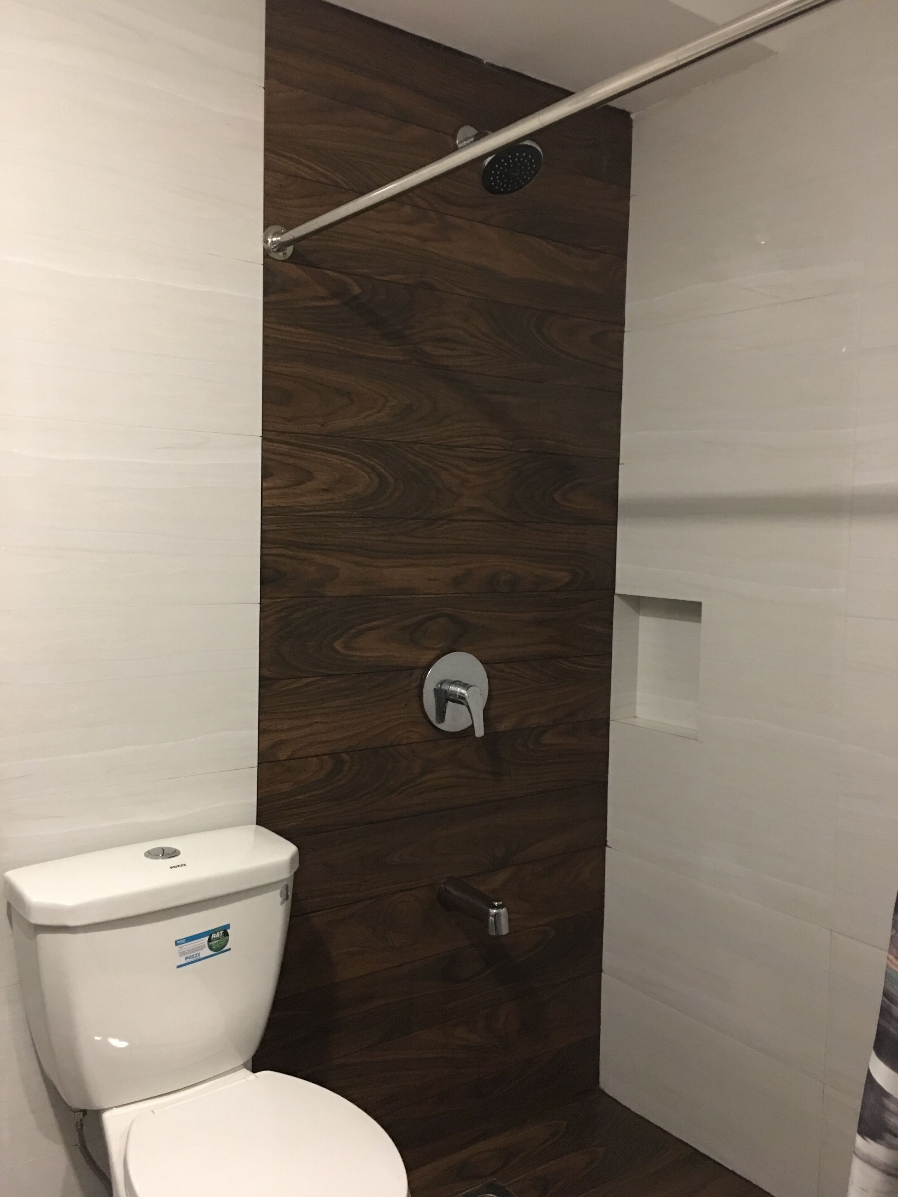 Un baño con un inodoro blanco, una ducha con pared de madera y un lavamanos blanco.