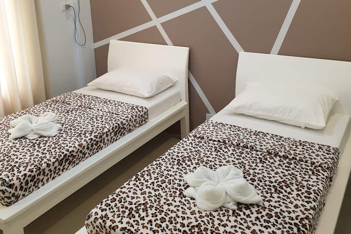 Twin beds with leopard print bedding and white pillows, a wall-mounted air conditioning unit, and a simple geometric wall design.
