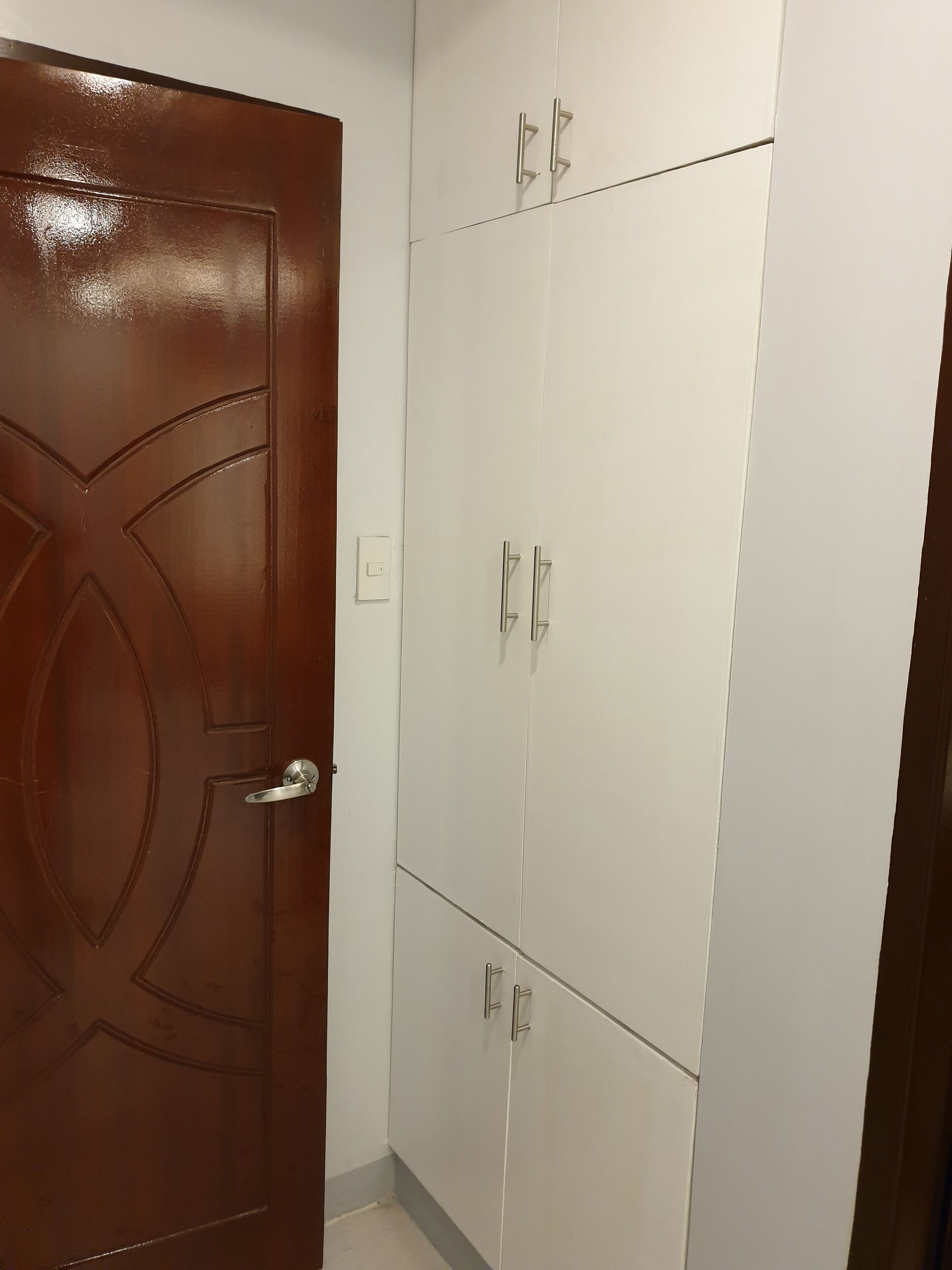 Habitación con puerta de madera y paredes de azulejos blancos, que presenta una distribución sencilla con una puerta y un pequeño interruptor de luz.