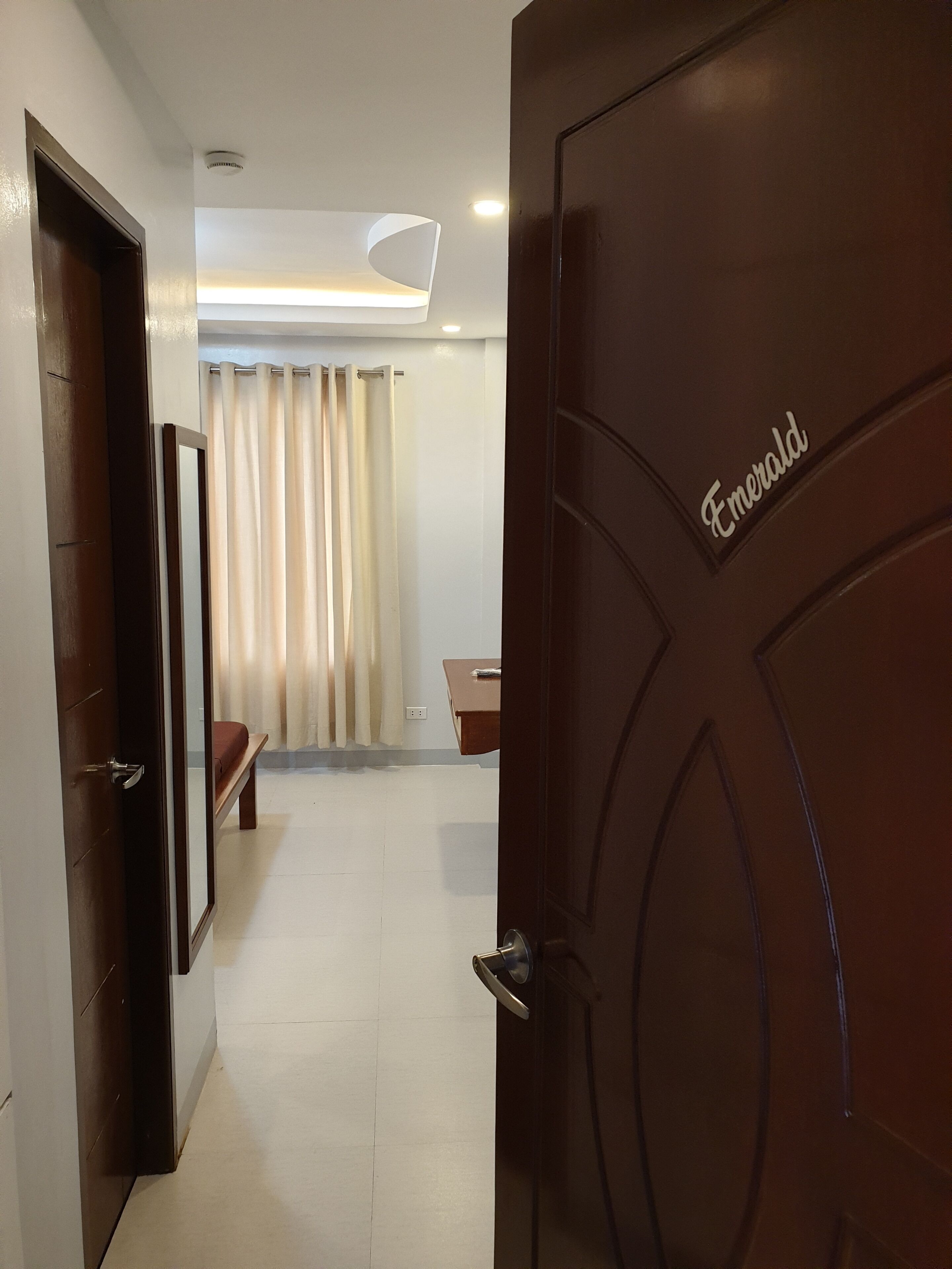 A hallway leading to a room with a bed, a small table, and a curtain.