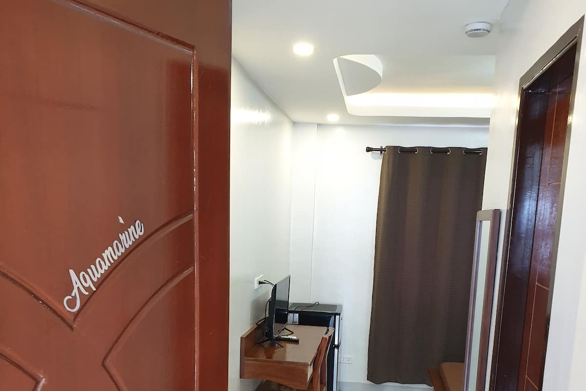 A hotel room with a wooden door labeled "Aquamarine," a desk with a computer, a chair, and a small table.