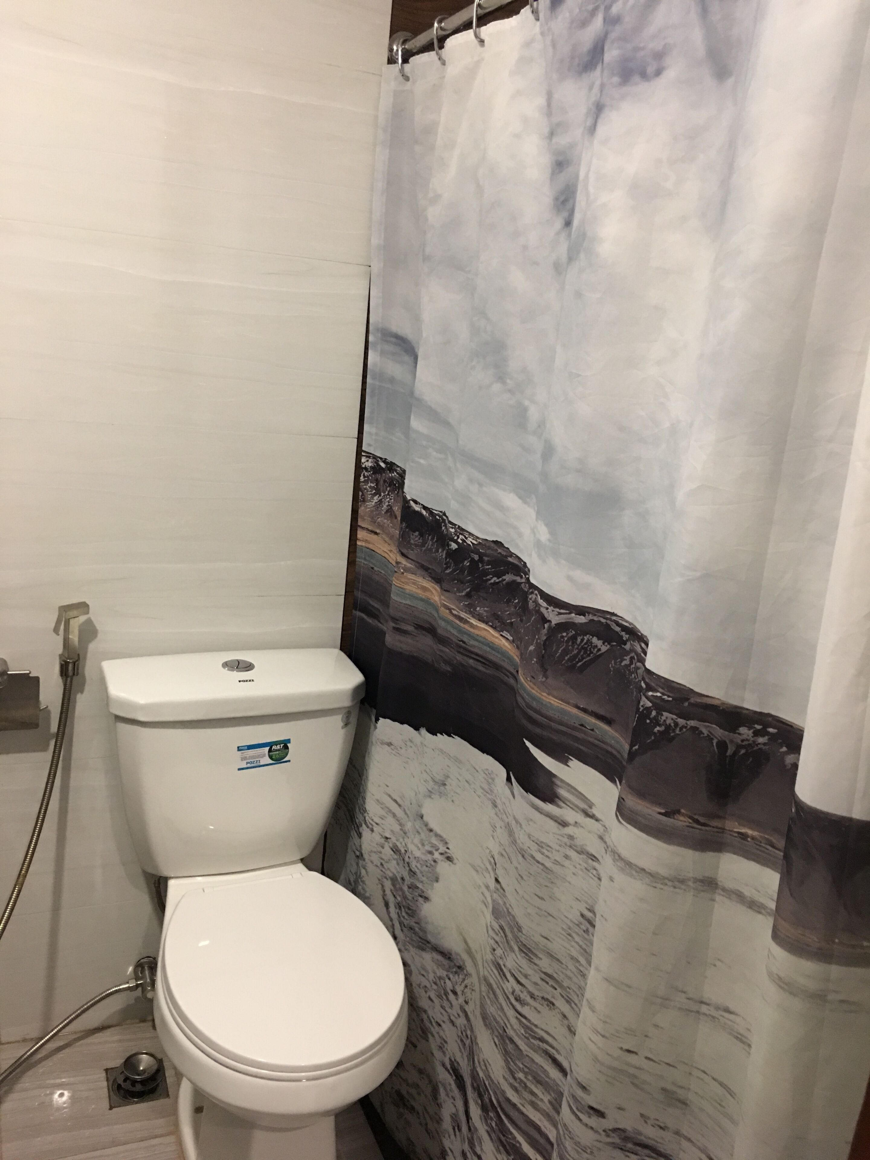 A bathroom with a toilet, shower curtain, and a visible drain.