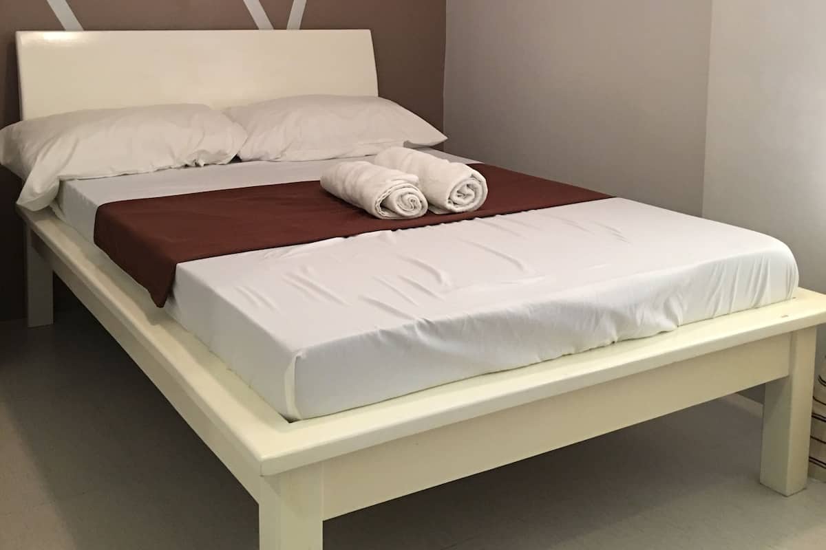 A single bed with white linens, a brown blanket, and two rolled towels.