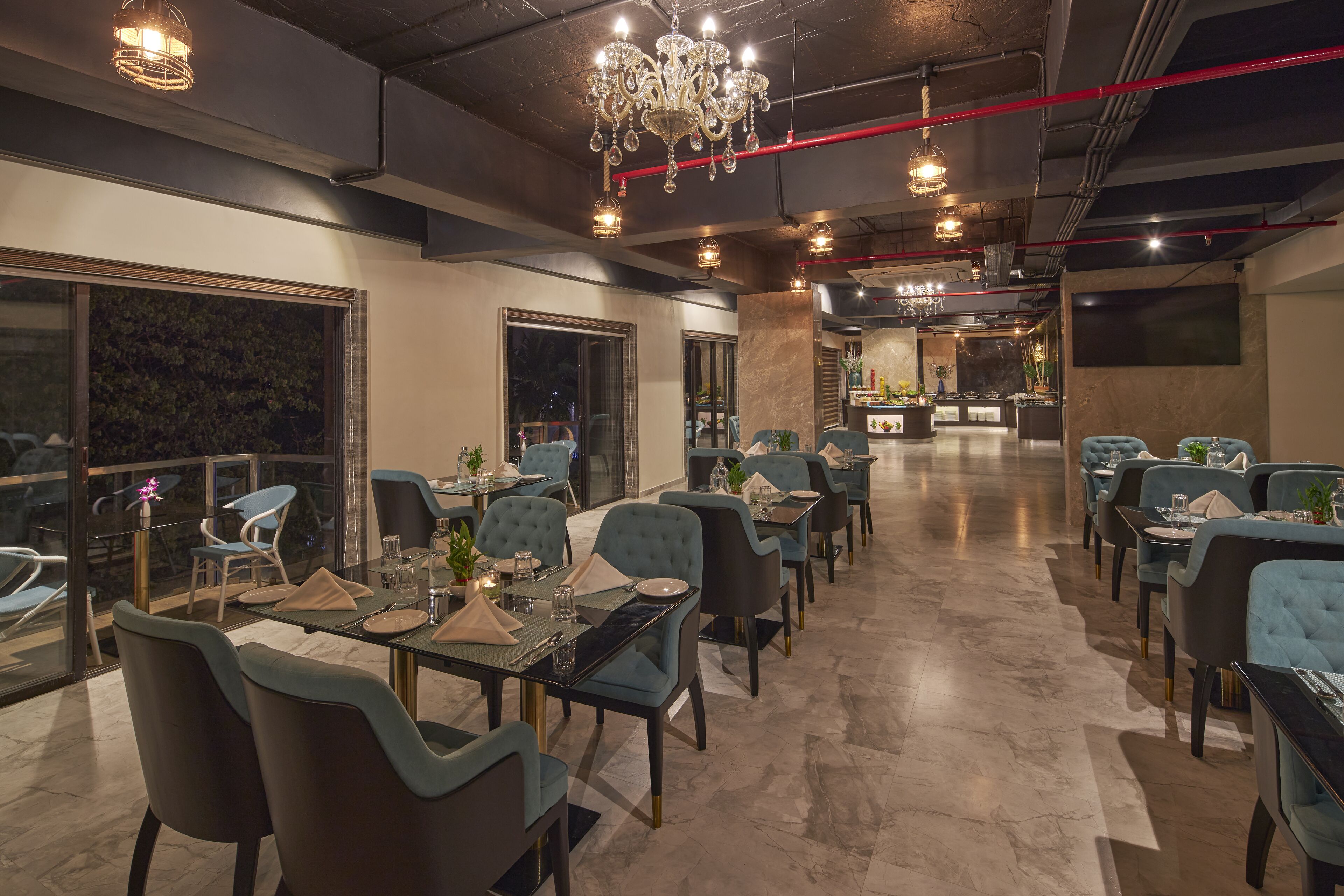 A modern restaurant with a long dining area, large windows, and a chandelier.