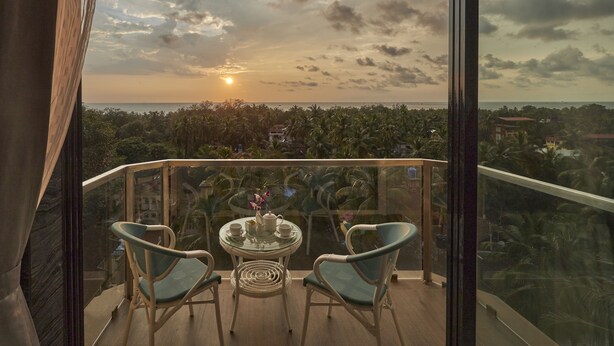 A balcony with two chairs and a table, overlooking a scenic view of the sunset and a cityscape. - Regenta Central Imperial Candolim Goa (Candolim)