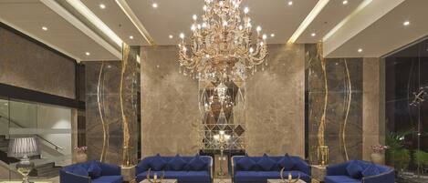A lobby with a grand chandelier, marble walls, and blue sofas.