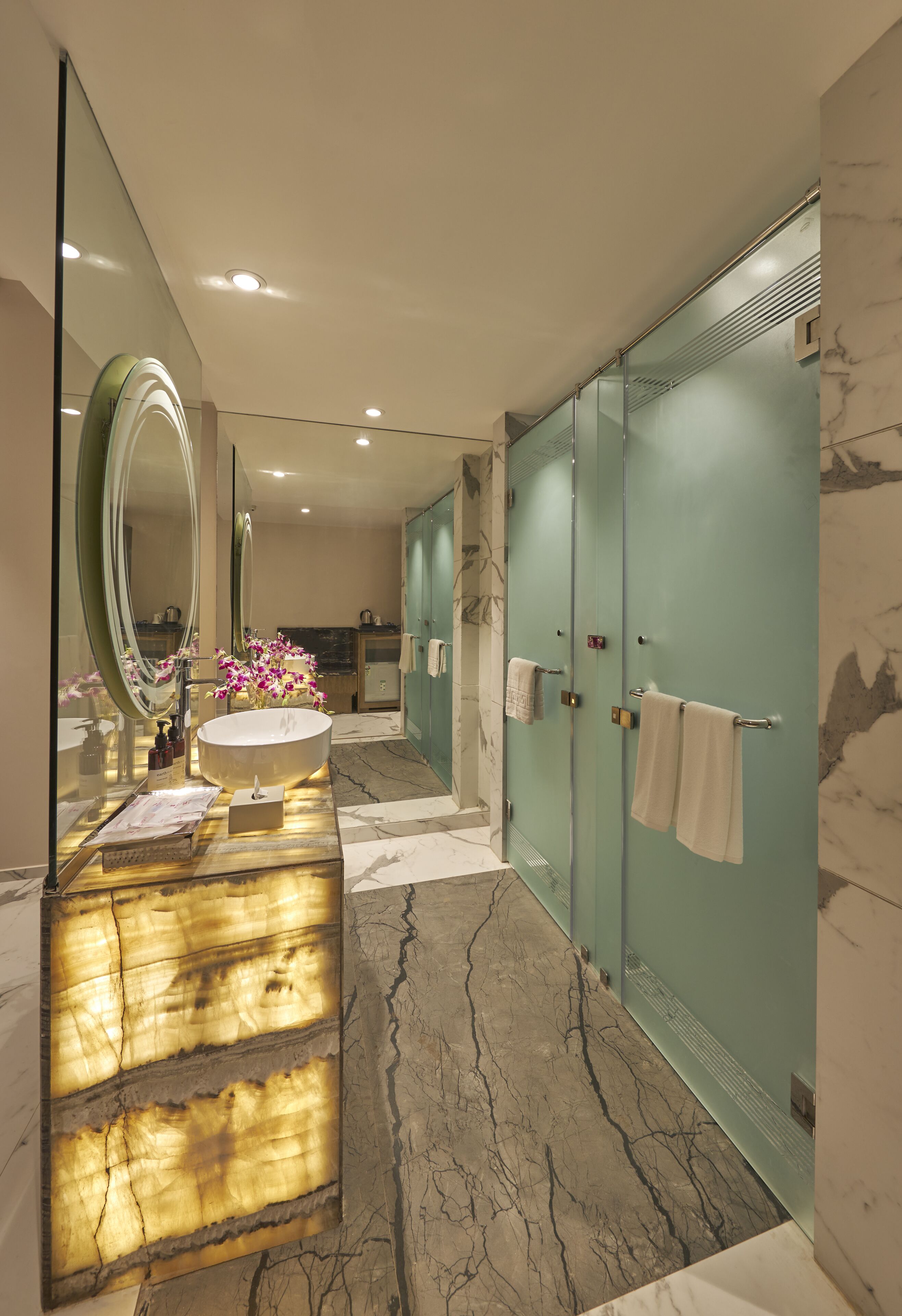 A modern bathroom with a large mirror, a round sink, and marble flooring.