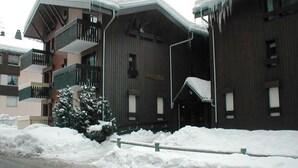 A building with a wooden facade, multiple balconies, and a snow-covered ground. - 4/6 PERSON RENTAL - LE FAYARD- 800M FROM THE CENTER (Arâches-la-Frasse)