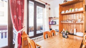 A dining area with a wooden table, chairs, a radiator, and a shelf with kitchenware. - 4/6 PERSON RENTAL - LE FAYARD- 800M FROM THE CENTER (Arâches-la-Frasse)
