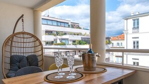 Un balcon avec une table en bois, des chaises jaunes et noires, un fauteuil suspendu et une bouteille de champagne.